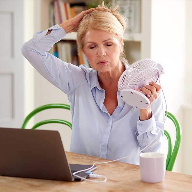 Middle aged woman trying to comfort a hotflash - Hormone Replacement Treatments by Skinworks Wellness