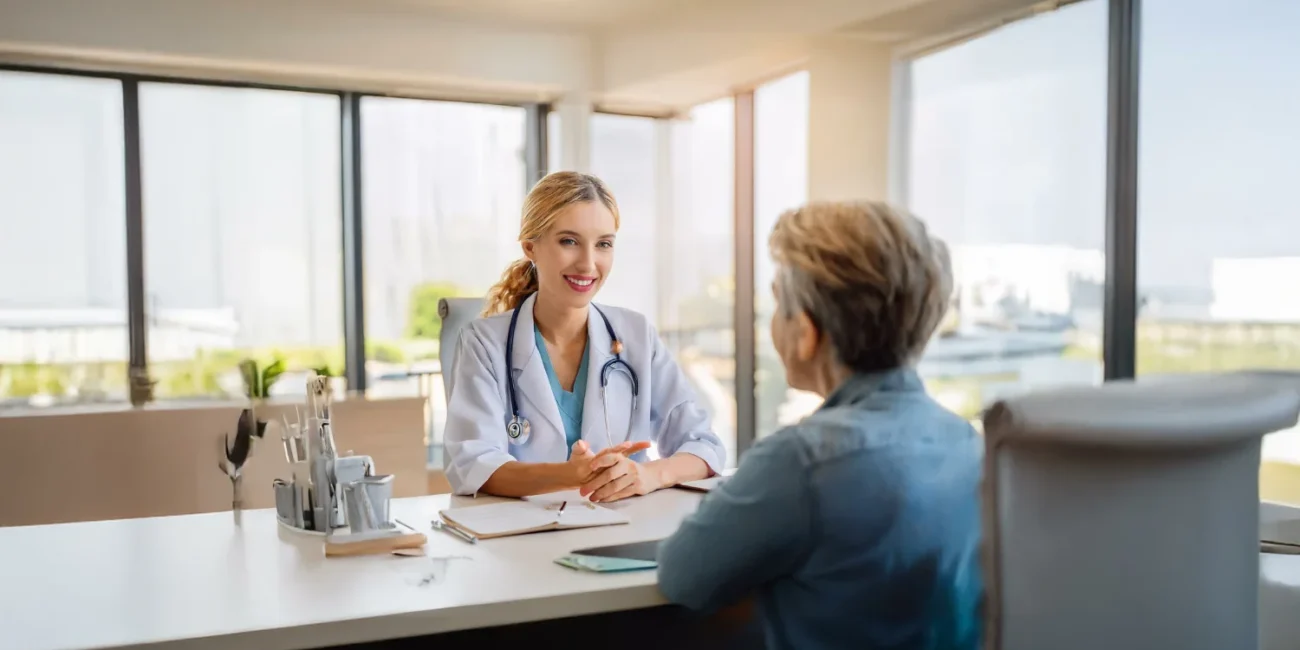A friendly doctor discusses a treatment, possibly vaginal microneedling, with a patient in a bright office.