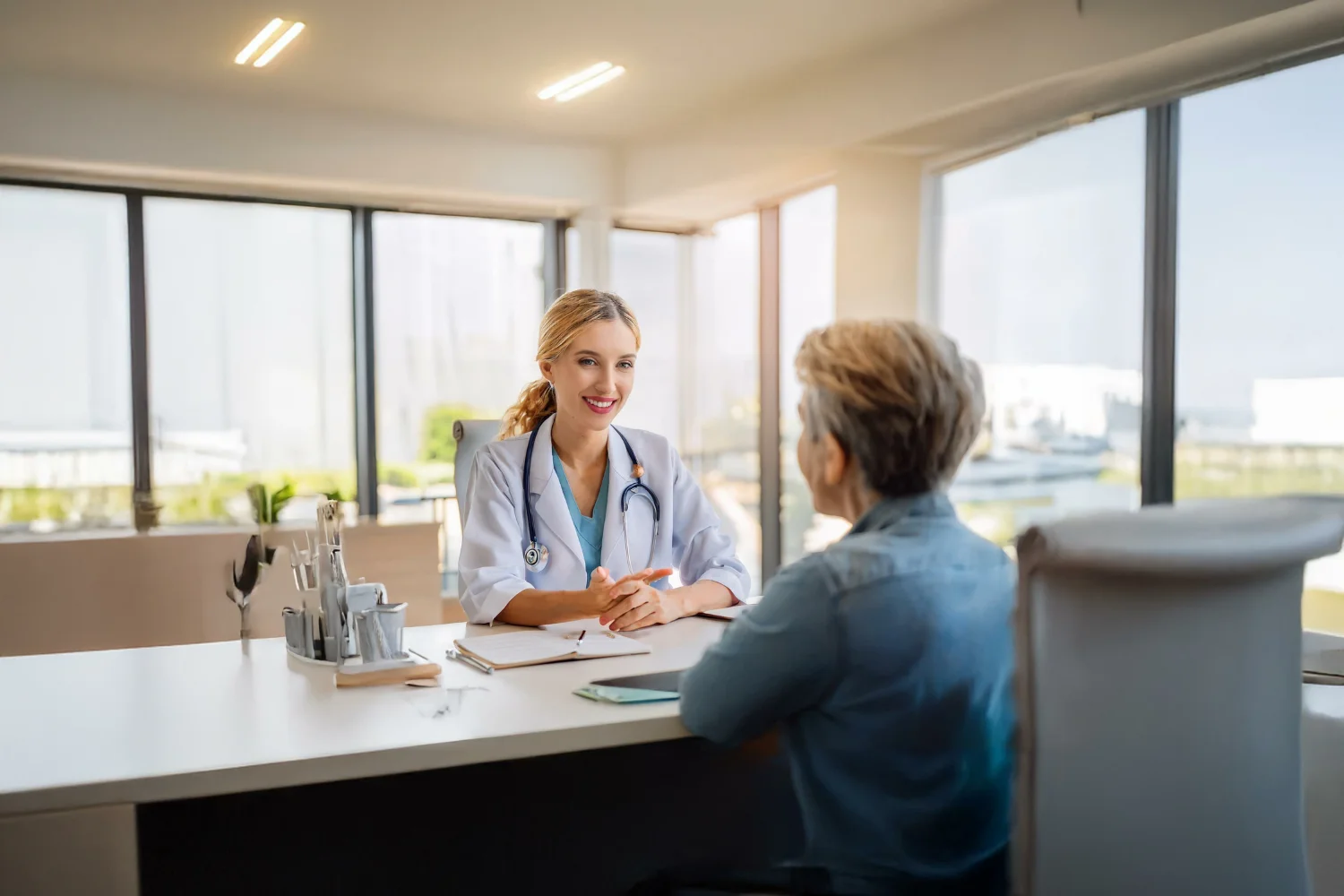 A friendly doctor discusses a treatment, possibly vaginal microneedling, with a patient in a bright office.