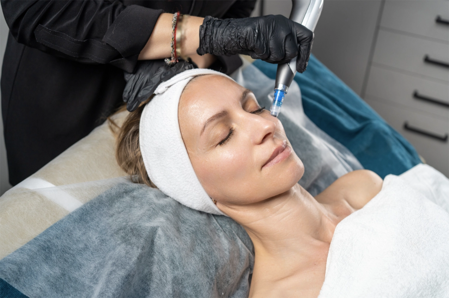 Client receiving professional microneedling facial treatment with handheld device in skincare clinic
